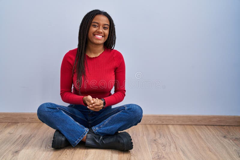 Joven afroamericano con trenzas sentadas en casa con las manos juntas y los dedos cruzados sonriendo relajados y imagen de archivo libre de regalías