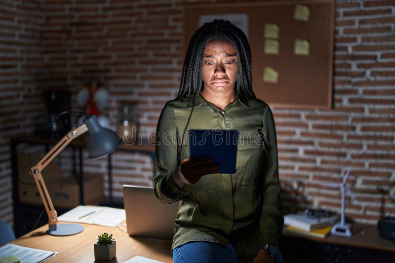 Joven afroamericano con trenzas trabajando en la oficina por la noche deprimido y preocupado por la angustia llorando enojado y as fotografía de archivo libre de regalías