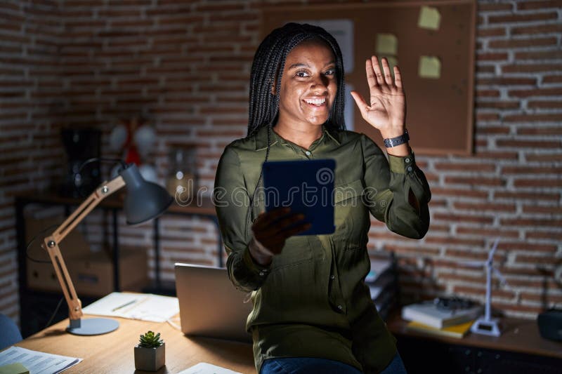 Joven afroamericano con trenzas trabajando en la oficina por la noche sin decir hola feliz y sonriente gesto de bienvenida foto de archivo