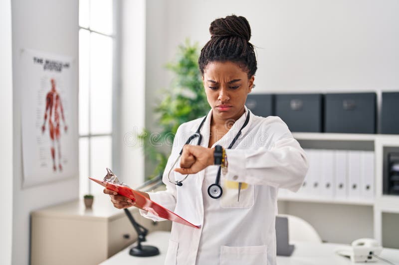 Joven afroamericano con trenzas con uniforme médico mirando al reloj escéptico y nerviosa frunciendo el ceño debido a imagenes de archivo