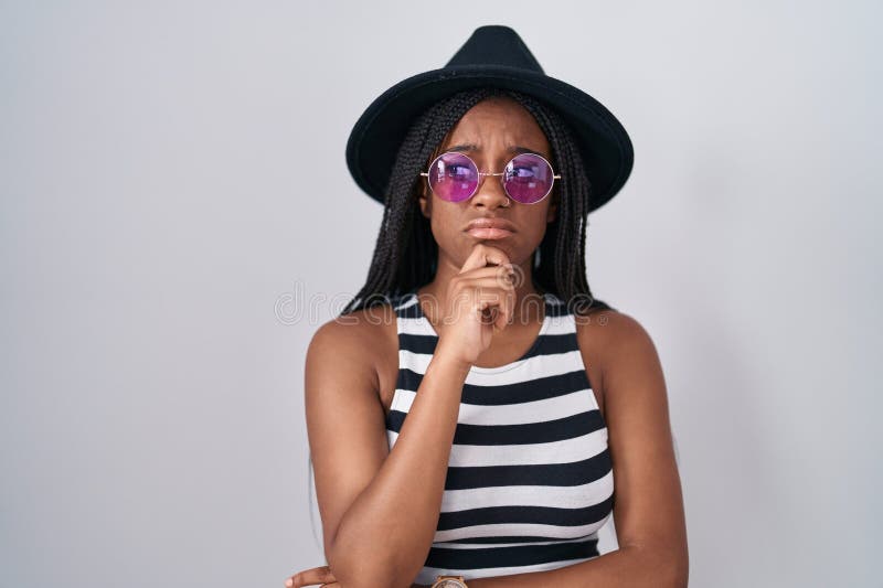Joven afroamericano con trenzas usando sombrero y gafas de sol pensando en una pregunta preocupada y nerviosa con la mano foto de archivo libre de regalías