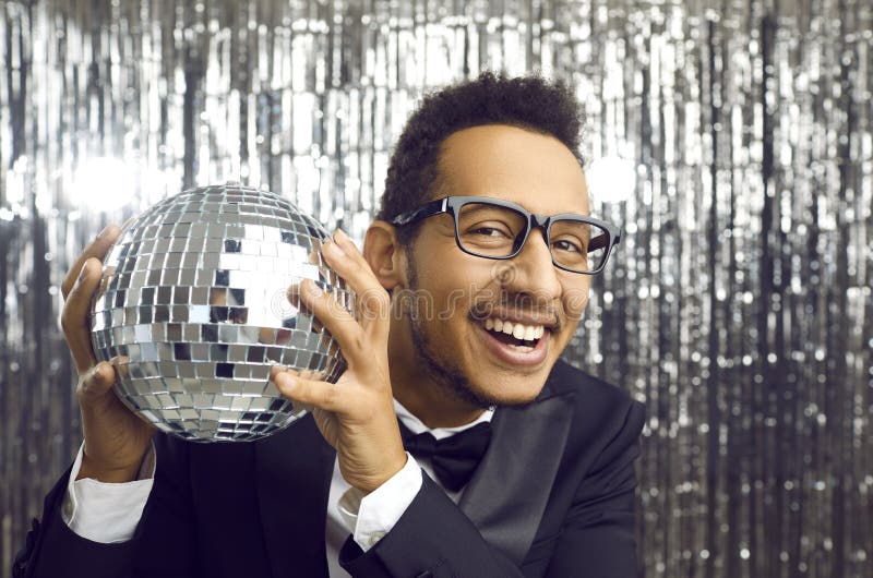 Joven afroamericano feliz con traje y gafas sosteniendo una bola de disco y sonriendo imágenes de archivo libres de regalías