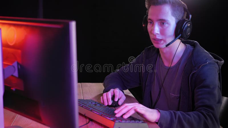 Joven apuesto pro gamer jugando en videojuegos en línea habla con los jugadores del equipo a través de micrófono. metrajes