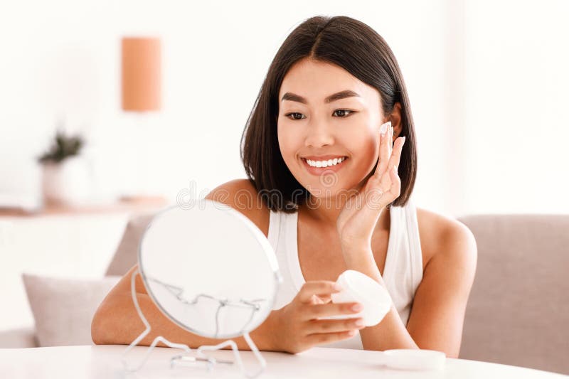 Joven asiática aplicando crema en su cara fotografía de archivo