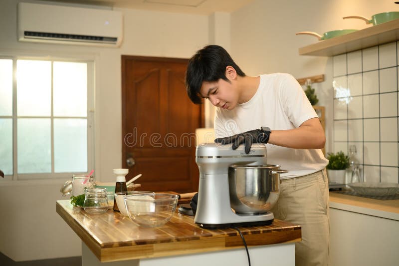 Joven asiático preparando crema batida con una mesa de mezclas en la cocina fotos de archivo libres de regalías