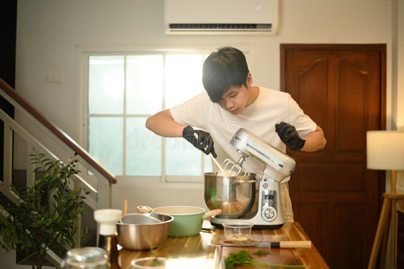 Joven asiático preparando crema batida con una mesa de mezclas en la cocina fotografía de archivo