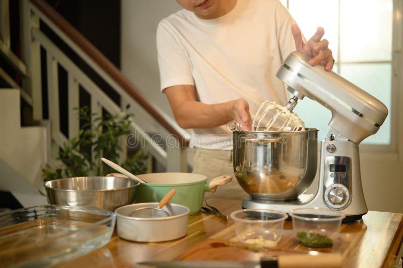 Joven asiático usando un mezclador para crema de látigo en una cocina moderna y brillante foto de archivo