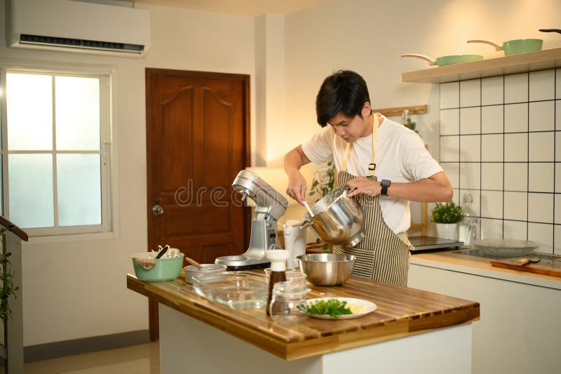Joven asiático usando un mezclador para crema de látigo en una cocina moderna y brillante fotos de archivo