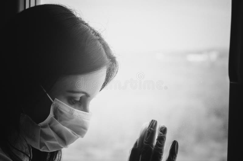 Joven caucásica con pelo oscuro en protección de virus médicos máscara facial y guante cerca de la ventana. cuarentena de selfisol imágenes de archivo libres de regalías