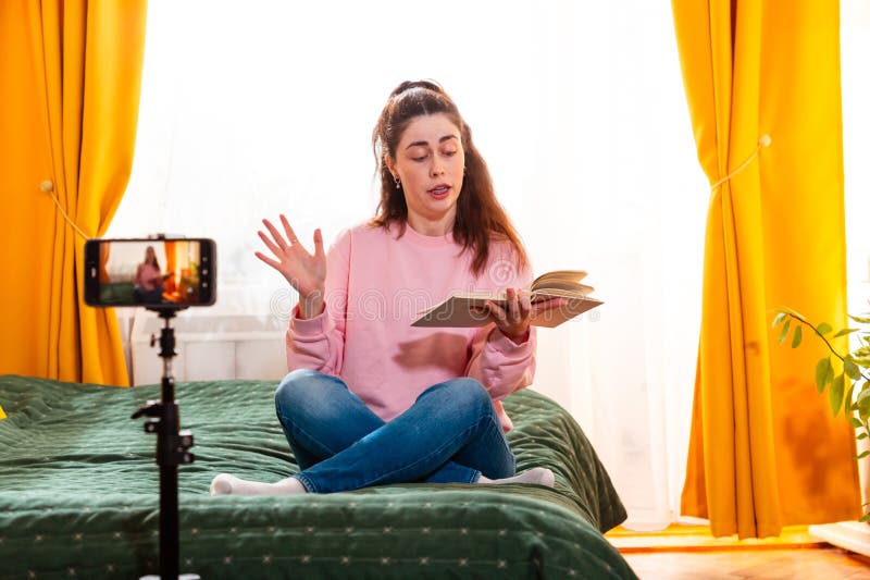 Joven caucásica grabándose en su casa sentada en una cama creando contenido digital para sus medios sociales fotos de archivo libres de regalías