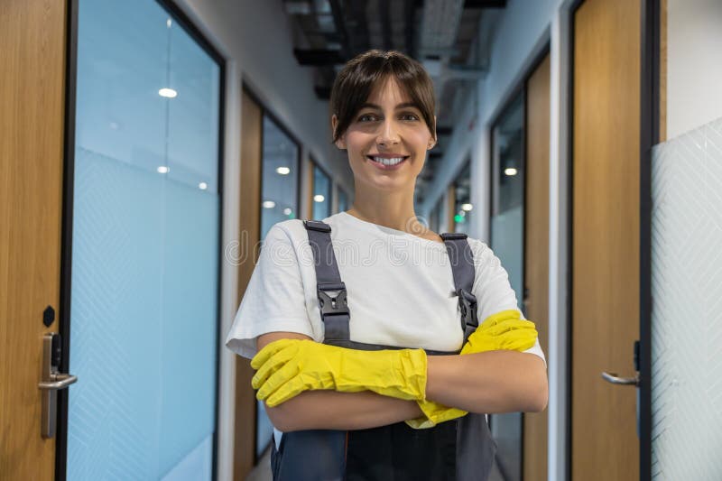 Joven caucásica sonriente de pelo oscuro del equipo de limpieza de guantes amarillos con aspecto confiado imagen de archivo