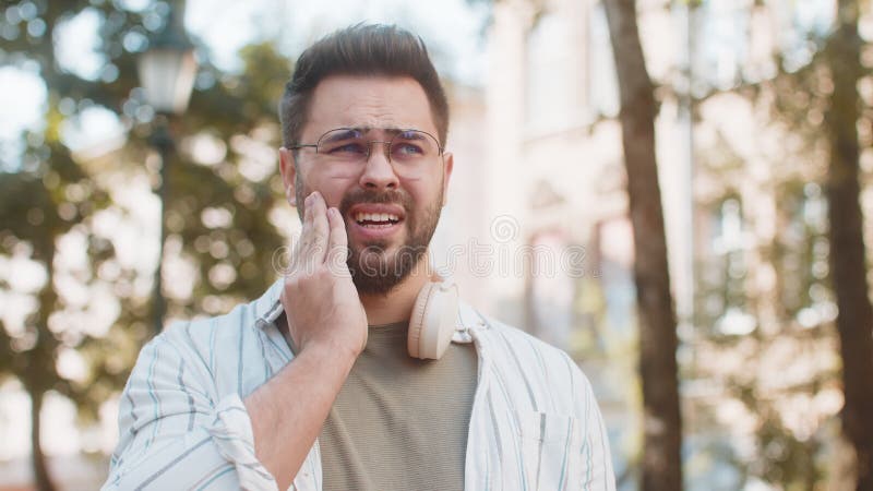 Joven caucásico sintiendo dolor de muelas malos síntomas desagradables padeciendo dolor de pie en la calle almacen de video