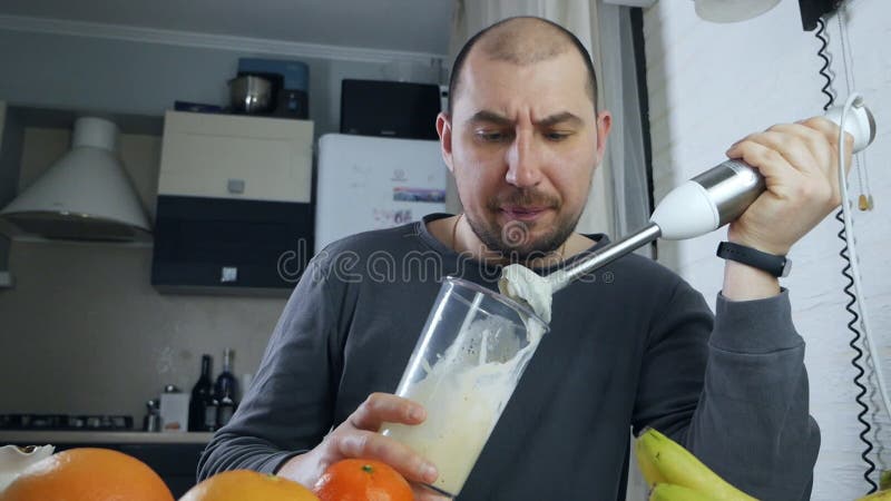 Joven con licuadora preparando coctel de frutas en casa cocina metrajes