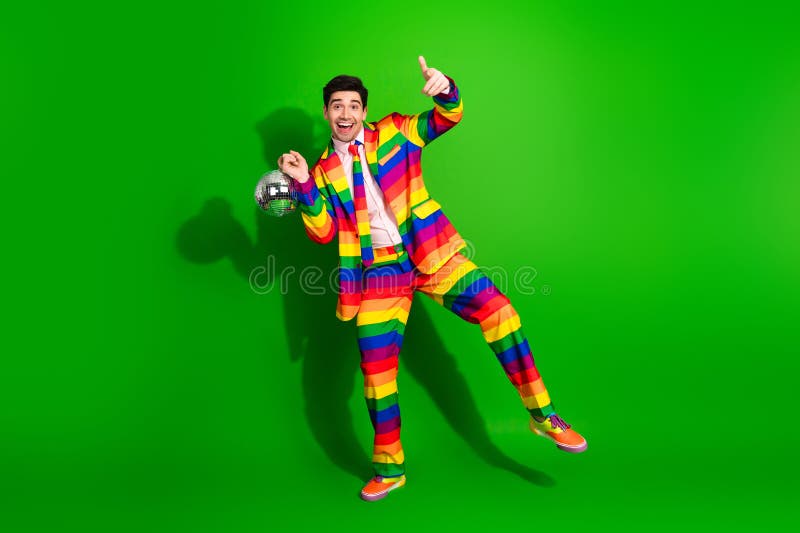 Joven con un colorido traje de rayas que posa con entusiasmo sobre un fondo verde brillante mientras sostiene una discoteca foto de archivo