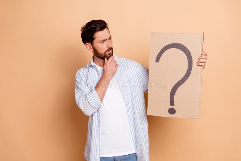 Joven con un signo de interrogación hecho de cartón reflexionando sobre un fondo beige imágenes de archivo libres de regalías