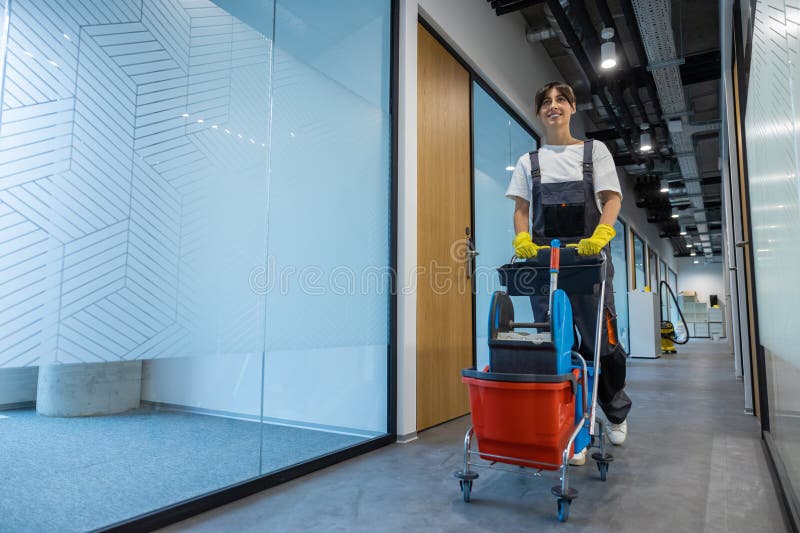 Joven de cabello oscuro con uniforme y un carro de limpieza foto de archivo libre de regalías