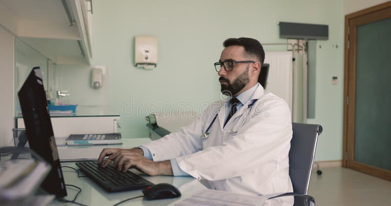 Joven doctor hispano serio trabajando en una computadora metrajes