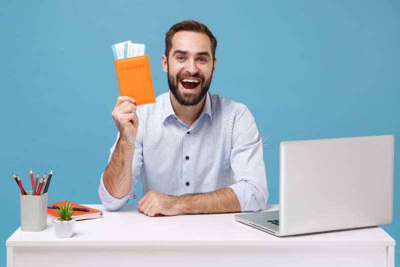Joven emocionado con camisa ligera sentarse a trabajar en un escritorio blanco con una laptop pc aislada en fondo azul pastel. log. concepto de carrera profesional. espacio de copia de simulación. retener pases de embarque.