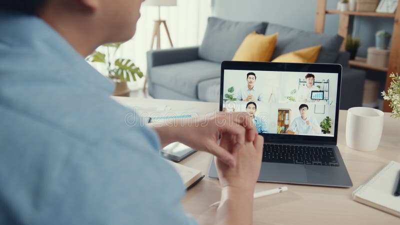 Joven empresario asiático usando laptop hable con colegas sobre plan en reunión de videollamadas mientras trabaja desde casa en sa almacen de metraje de vídeo