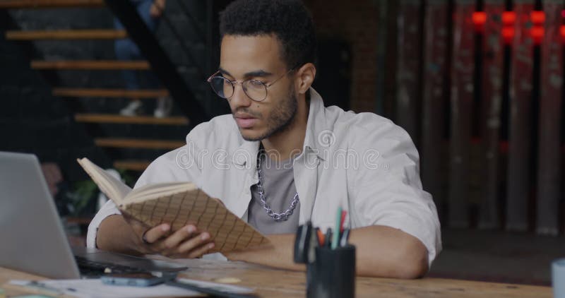 Joven empresario inteligente leyendo un libro sentado en el escritorio en un centro de coworking estilo loft