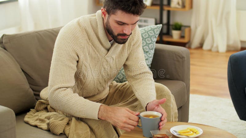 Joven enfermo en una manta tomando té caliente en casa metrajes