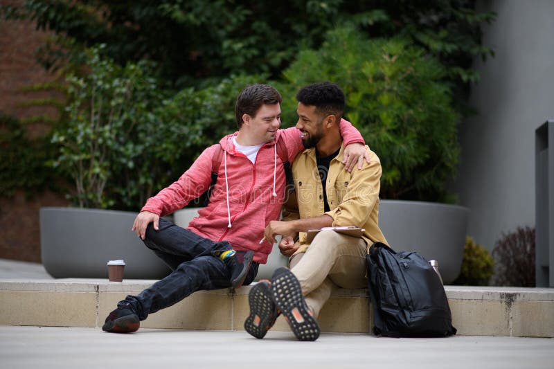 Joven feliz con síndrome de Down y un amigo mentor sentado y hablando al aire libre pasando tiempo juntos. fotografía de archivo libre de regalías