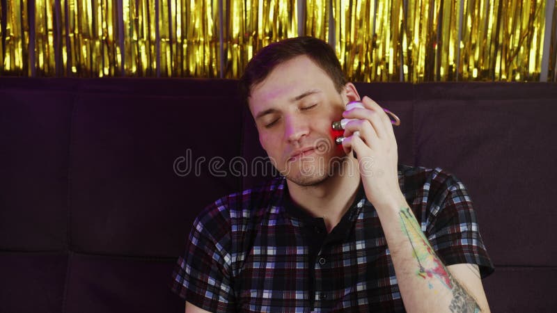 Joven feliz usando masajeador 3d para la cara. macho relajado con los ojos cerrados sentados en el sofá y usando el masajeador elé