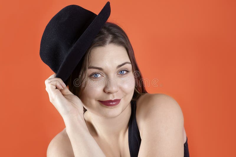 Joven guapa morena caucásica con ojos azules brillantes y labios oscuros, en ropa interior negra informal, levanta el sombrero, j fotografía de archivo libre de regalías Joven guapa morena caucásica con ojos azules brillantes y labios oscuros, en ropa interior negra informal, levanta el sombrero, j fotografía de archivo libre de regalías