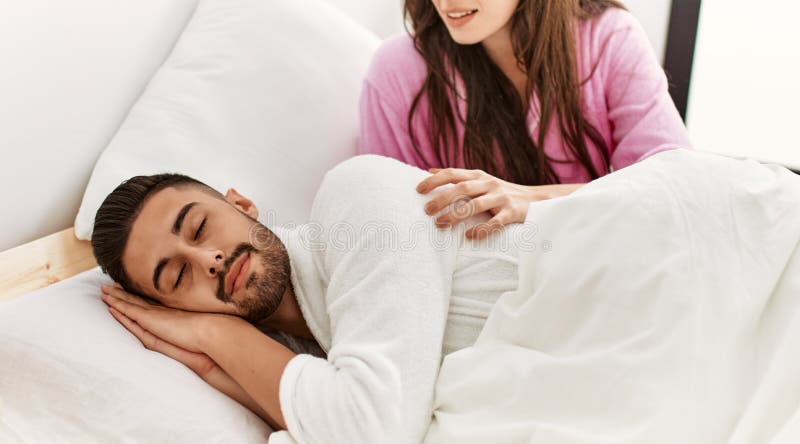 Joven hispana mirando a su somnoliento novio en la cama imágenes de archivo libres de regalías