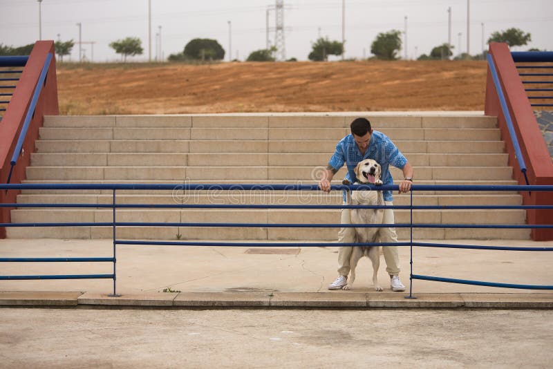 Joven hispano inclinado en una barandilla al lado de su perro en una actitud divertida. perros conceptivos animales de compañía am imagenes de archivo