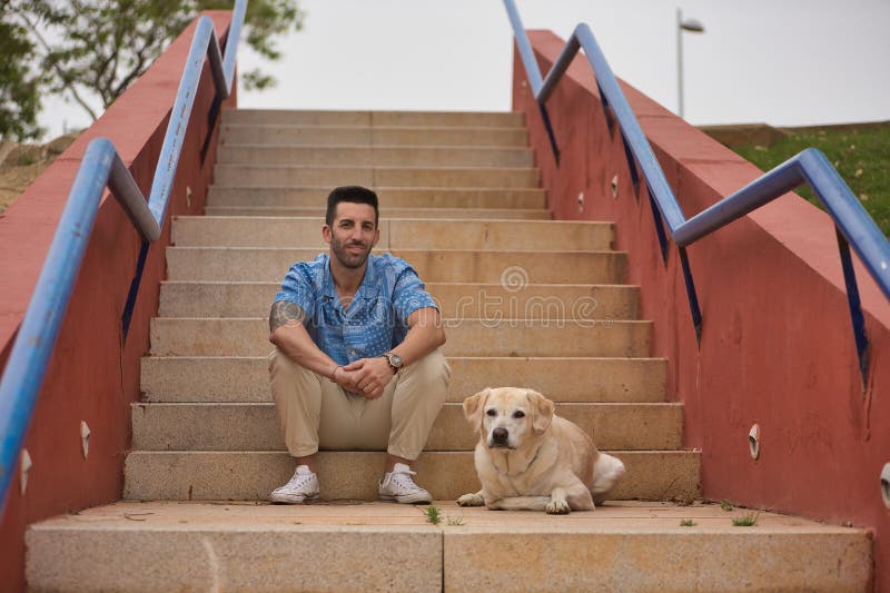 Joven hispano sentado en las escaleras al lado de su perro mientras mira la cámara. perros conceptivos animales de compañía amigos imágenes de archivo libres de regalías
