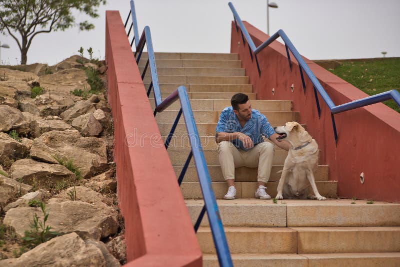 Joven hispano sentado en las escaleras de su perro mientras habla con él en una actitud amorosa y tierna. mascotas de perros conce imágenes de archivo libres de regalías