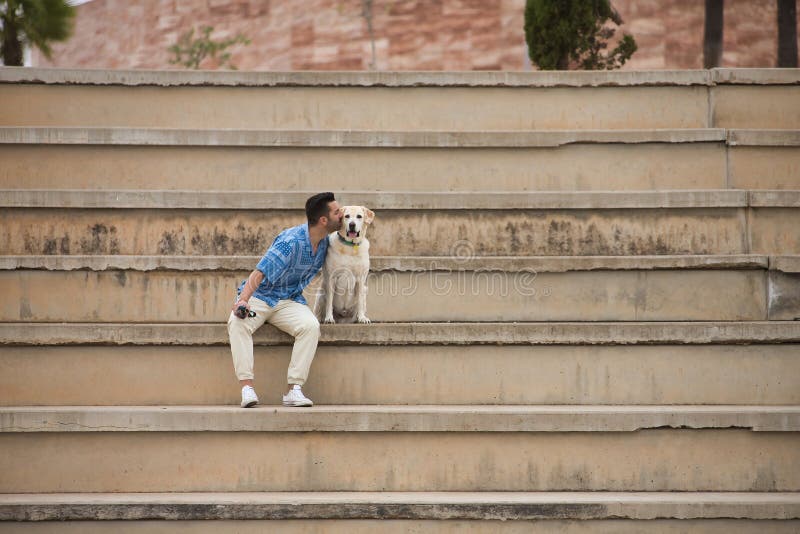 Joven hispano sentado en las grandes escaleras de cemento dando un beso a su perro en actitud amorosa y tierna. mascotas de perros imagenes de archivo
