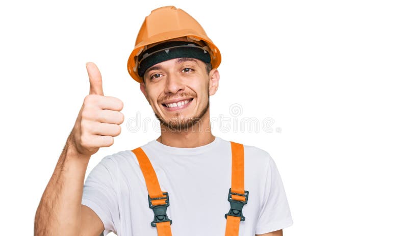 Joven hispano vestido con uniforme de mano y mano dura de seguridad sonriendo feliz y positivo pulgar arriba haciendo excelente y fotografía de archivo