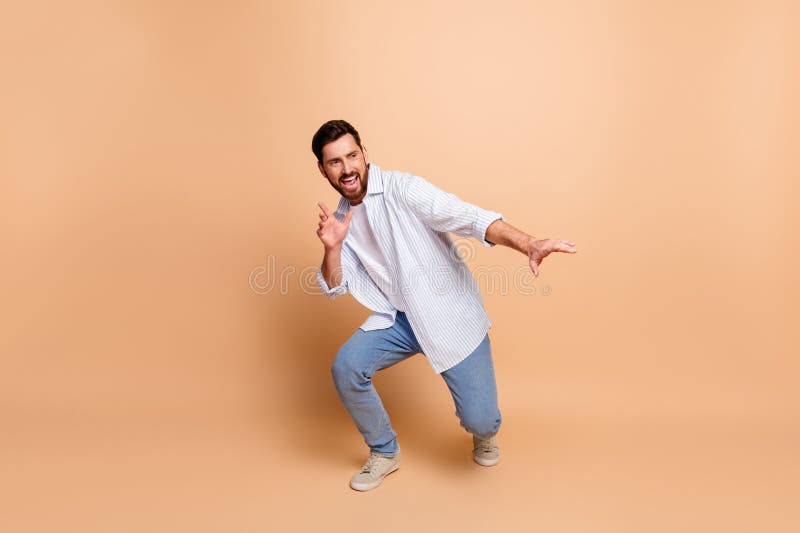 Joven hombre de diseño haciendo gestos juguetones en el fondo beige con camisetas casuales a rayas azules y jeans fotografía de archivo
