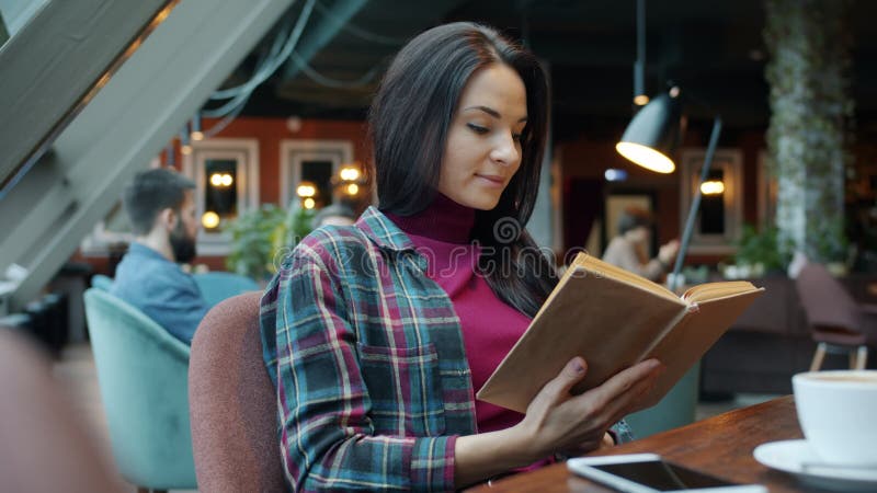Joven inteligente leyendo un libro disfrutando de la literatura sentada en la mesa en el café