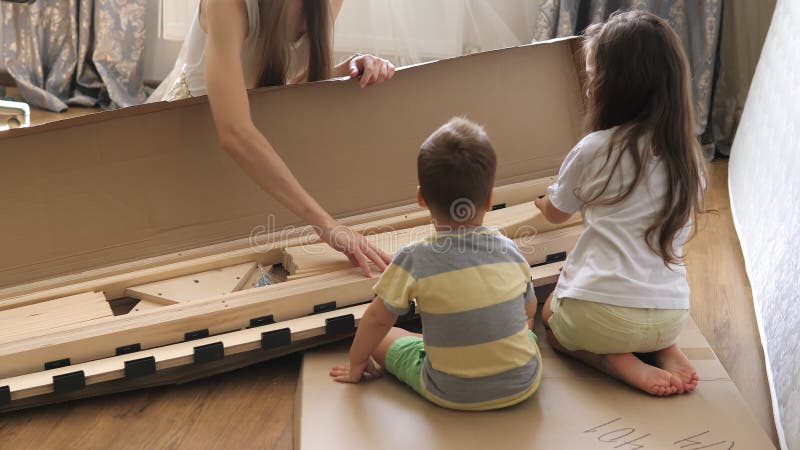 Joven madre soltera con hijos mirando el contenido de las cajas para la futura cama en el dormitorio de los niños. interior