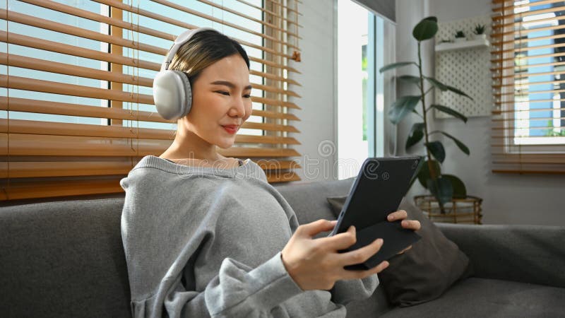 Joven mujer con auriculares sentada en una casa acogedora trabajando a distancia navegando por Internet en una tableta digital imágenes de archivo libres de regalías