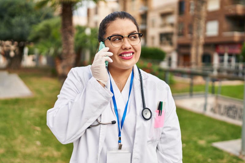 Joven mujer hermosa más grande doctor sonriente confiado hablando en el smartphone del parque fotografía de archivo