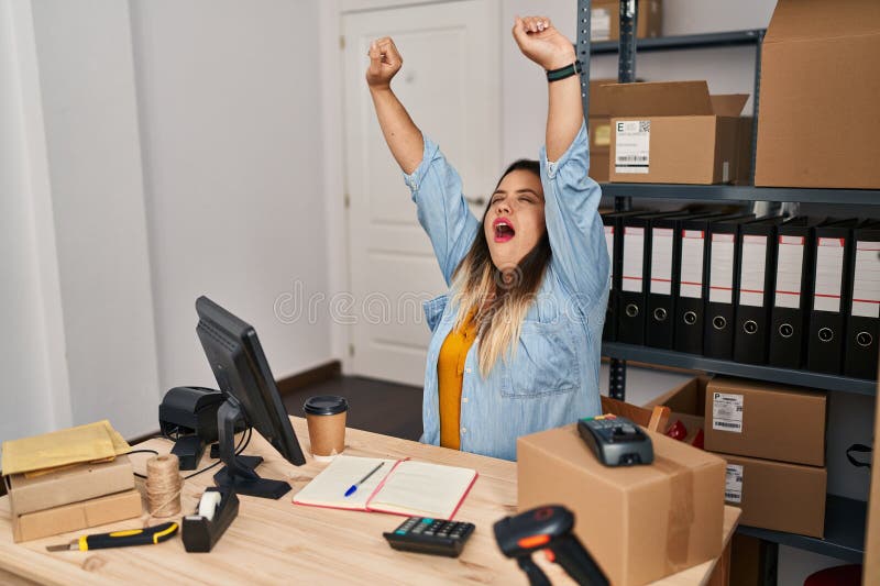 Joven mujer hermosa más grande mujer ecommerce empresaria estirando los brazos gritando en la oficina fotos de archivo