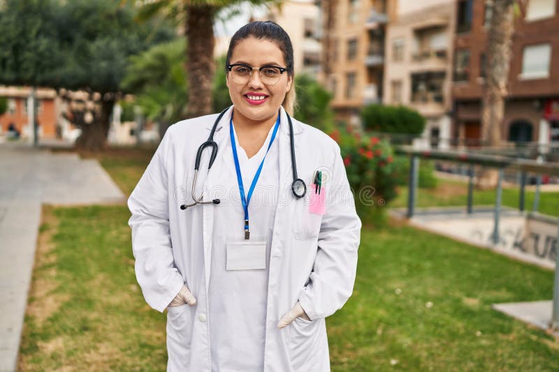 Joven mujer hermosa y de gran tamaño doctor sonriente confiado de pie en el parque foto de archivo