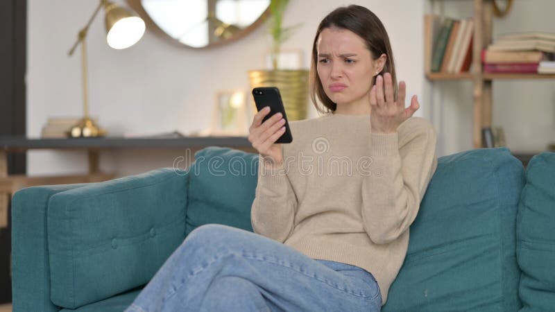 Joven mujer reaccionando a la pérdida en el teléfono inteligente en el sofá imagen de archivo libre de regalías