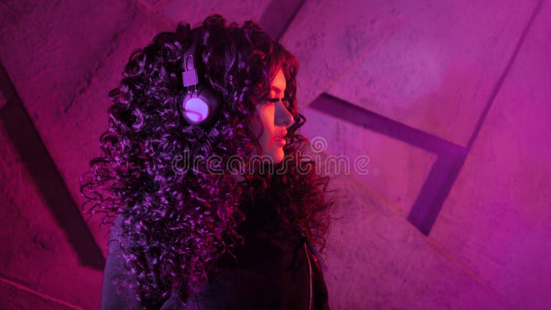 Joven mujer rizada en grandes audífonos escucha música, canta, baila en el fondo de una pared fotografía de archivo libre de regalías