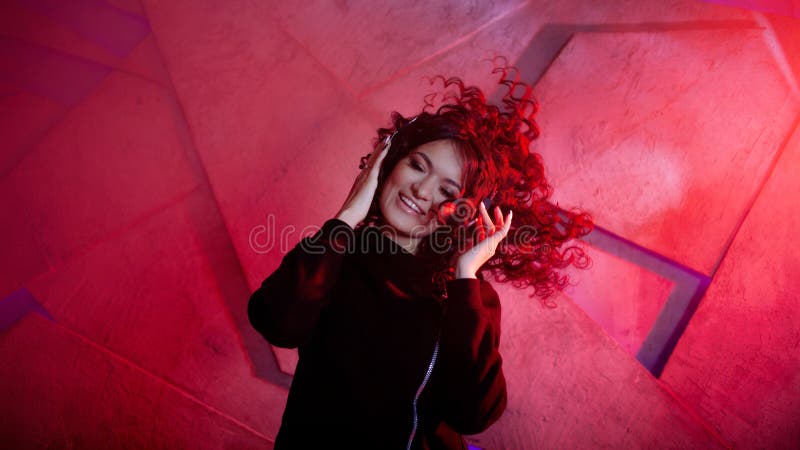 Joven mujer rizada en grandes audífonos sonríe, escucha música, canta, baila, salta, cierra los ojos foto de archivo libre de regalías