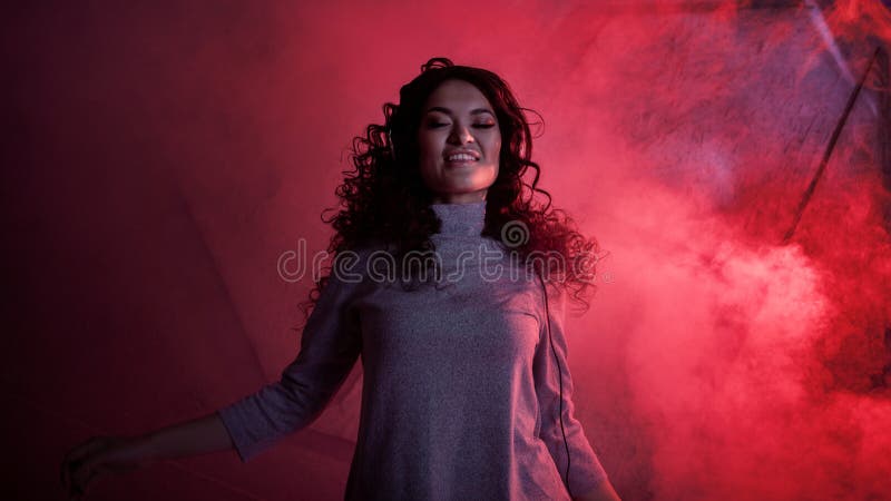 Joven mujer rizada en grandes audífonos sonríe, escucha música, canta, baila, salta, cierra los ojos imagen de archivo