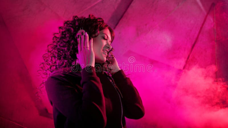 Joven mujer rizada en grandes audífonos sonríe, escucha música, canta, baila, salta, cierra los ojos imágenes de archivo libres de regalías