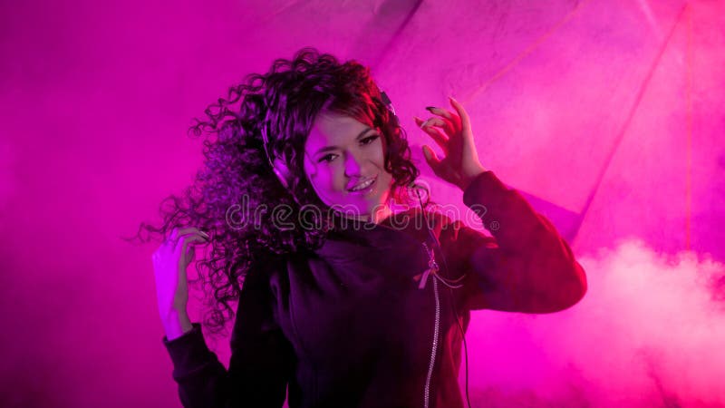 Joven mujer rizada en grandes audífonos sonríe, escucha música, canta, baila, salta, cierra los ojos fotos de archivo