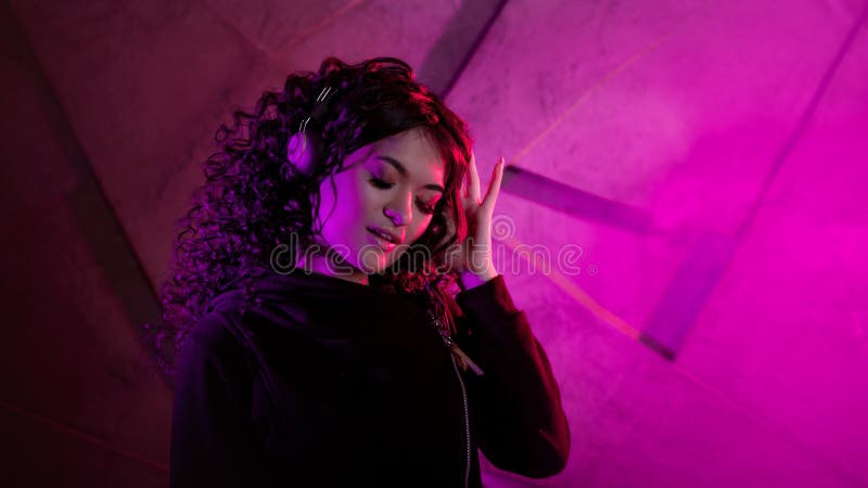 Joven mujer rizada en grandes audífonos sonríe, escucha música, canta, baila, salta, cierra los ojos foto de archivo libre de regalías