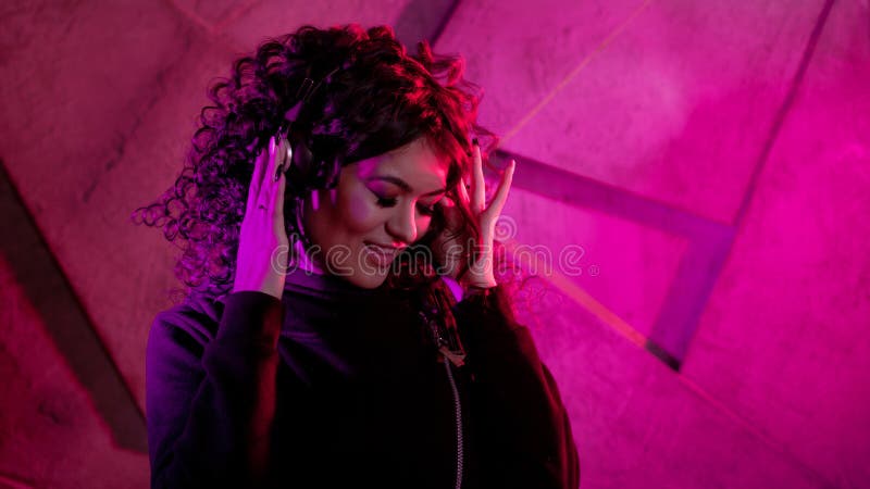 Joven mujer rizada en grandes audífonos sonríe, escucha música, canta, baila, salta, cierra los ojos fotografía de archivo