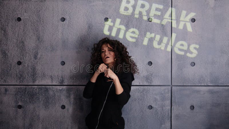 Joven mujer rizada en una fuerte pose de boxeo contra un fondo de pared de concreto. SeÃ±al de luz coloreada Rompa las reglas fotos de archivo